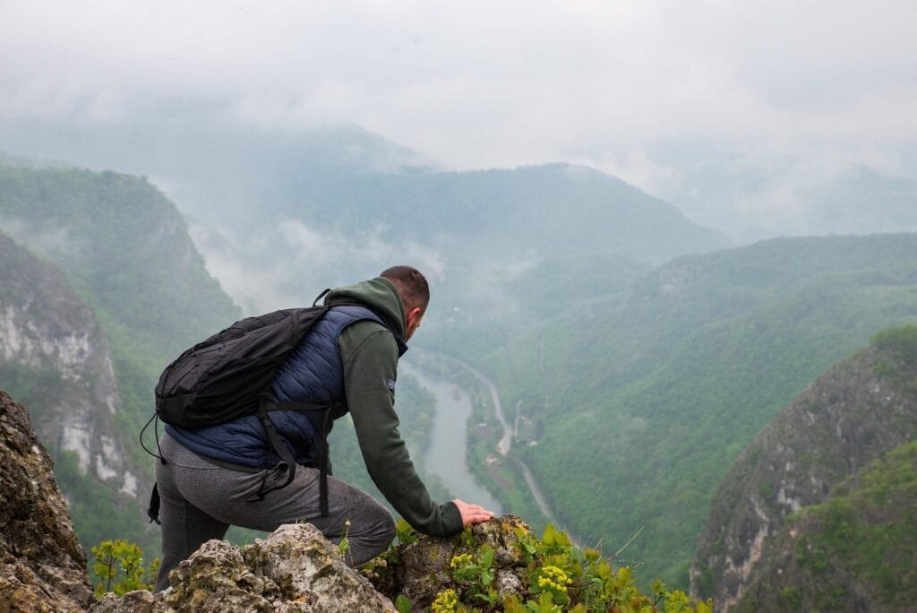 Un hombre que no tiene mucha seguridad viendo el abismo que hay hacia abajo de la montaña donde esta sin fijarse de donde se esta agarrando