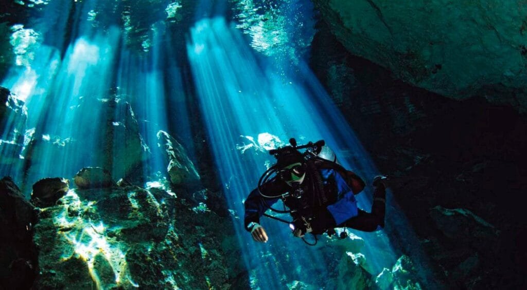 Una persona que esta buceando en algo parecido a un cenote o en las profundidades de una cueva y que porta un equipo adecuado para la situación