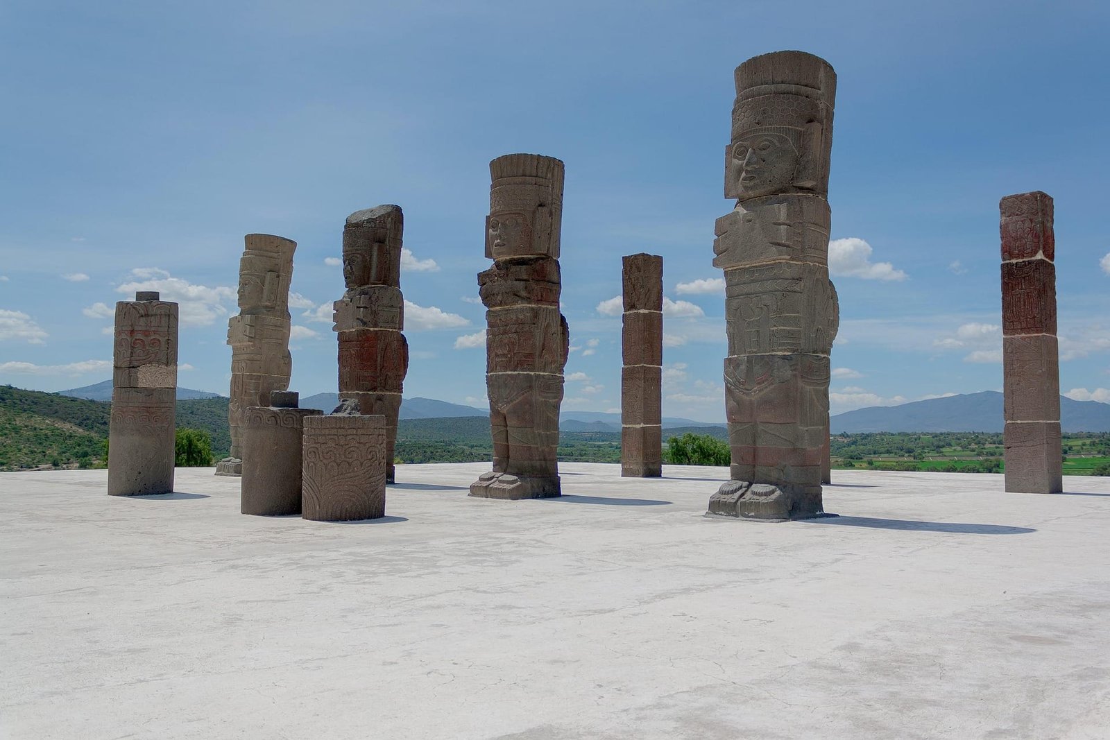 Unas estatuas históricas que representan guerreros y que se encuentran en una superficie plana con su alrededor un ecosistema lleno de arboles y un cielo despejado