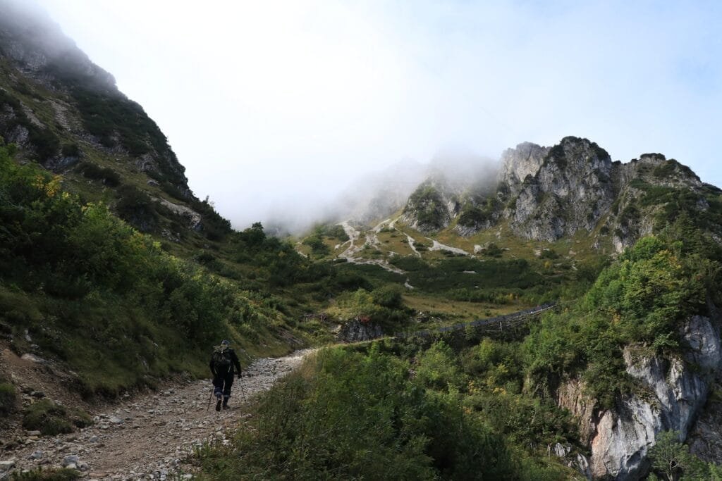 Un hombre que esta caminando, mientras que a su alrededor hay montañas y un poco de naturaleza como lo puede ser musgo en las montañas