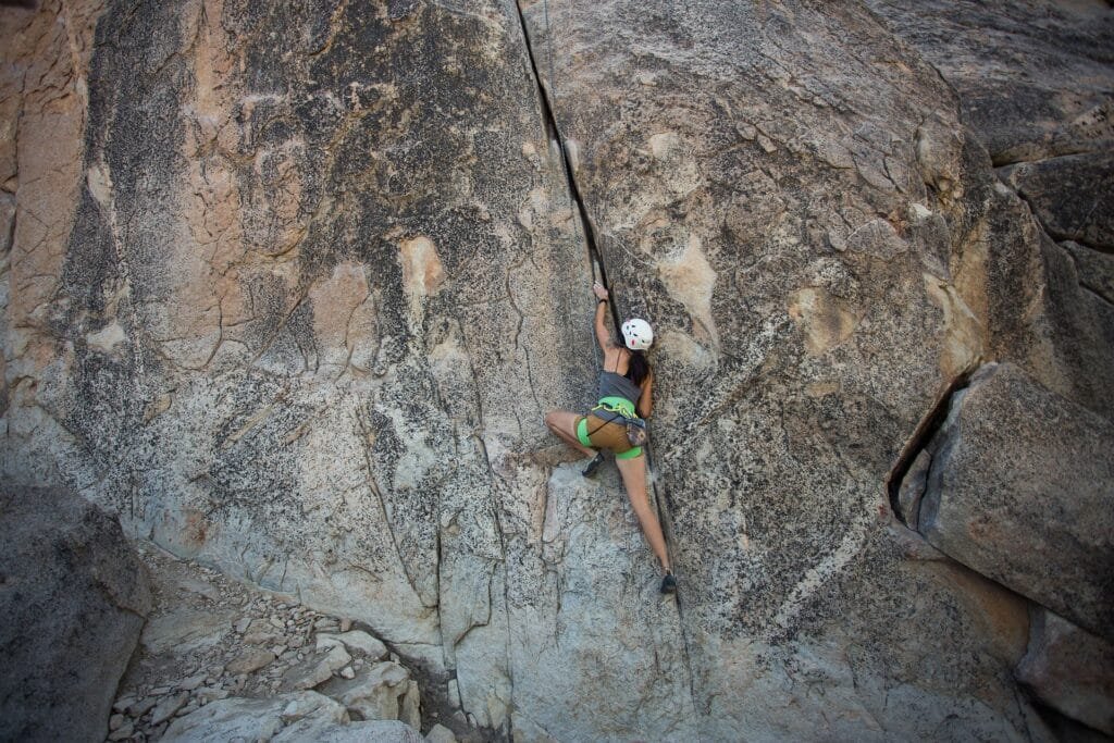 Una chica que esta escalando una montaña con lo que se puede notar el equipo necesario como su caso, su cuerda para sujetarse a grandes alturas y una pequeña bolsa que no resulta muy pesada donde lleva cosas para emergencia